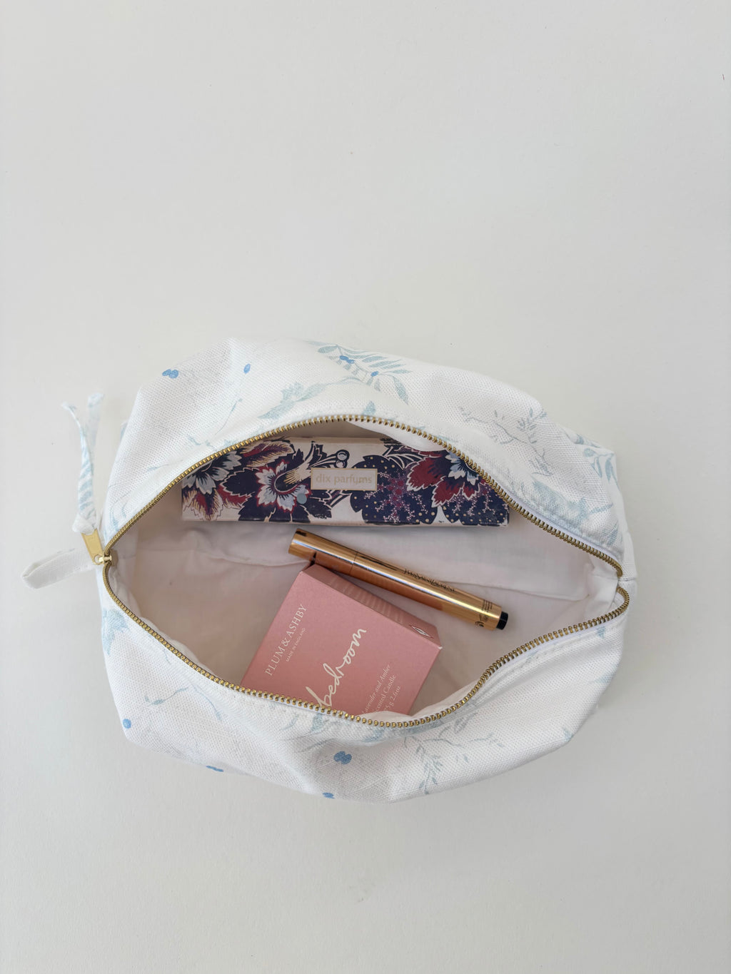 Floral-patterned makeup bag with items on a light background in aimee bleu design