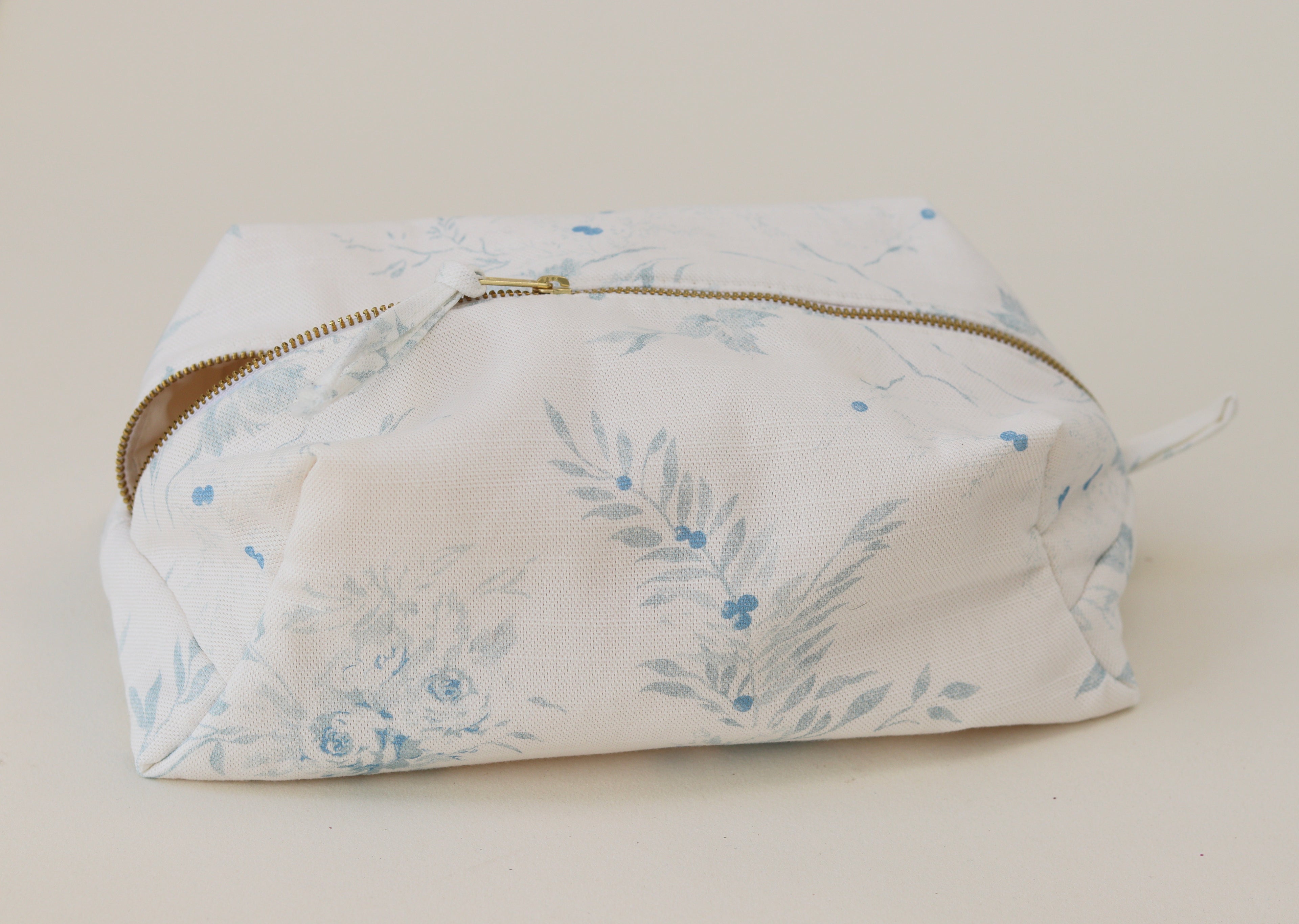 Floral-patterned pouch with a gold zipper on a light background by the faded floral company.